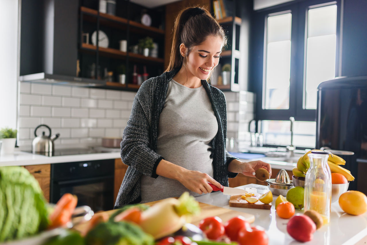 Young beautiful pregnant woman preparing healthy meal with fruites and vegetables getty images 1153041479