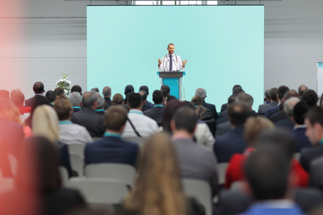 Male doctor giving a speech on a podium at a conference in front of an audience